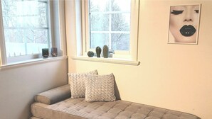 A cozy room with a grey sofa, two patterned cushions, and a window with decorative vases.