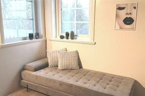 Une pièce chaleureuse avec un canapé gris, deux coussins à motifs et une fenêtre agrémentée de vases décoratifs.