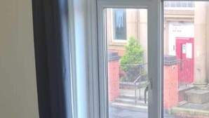Una ventana con vista a un edificio con puerta roja y pared de ladrillo.