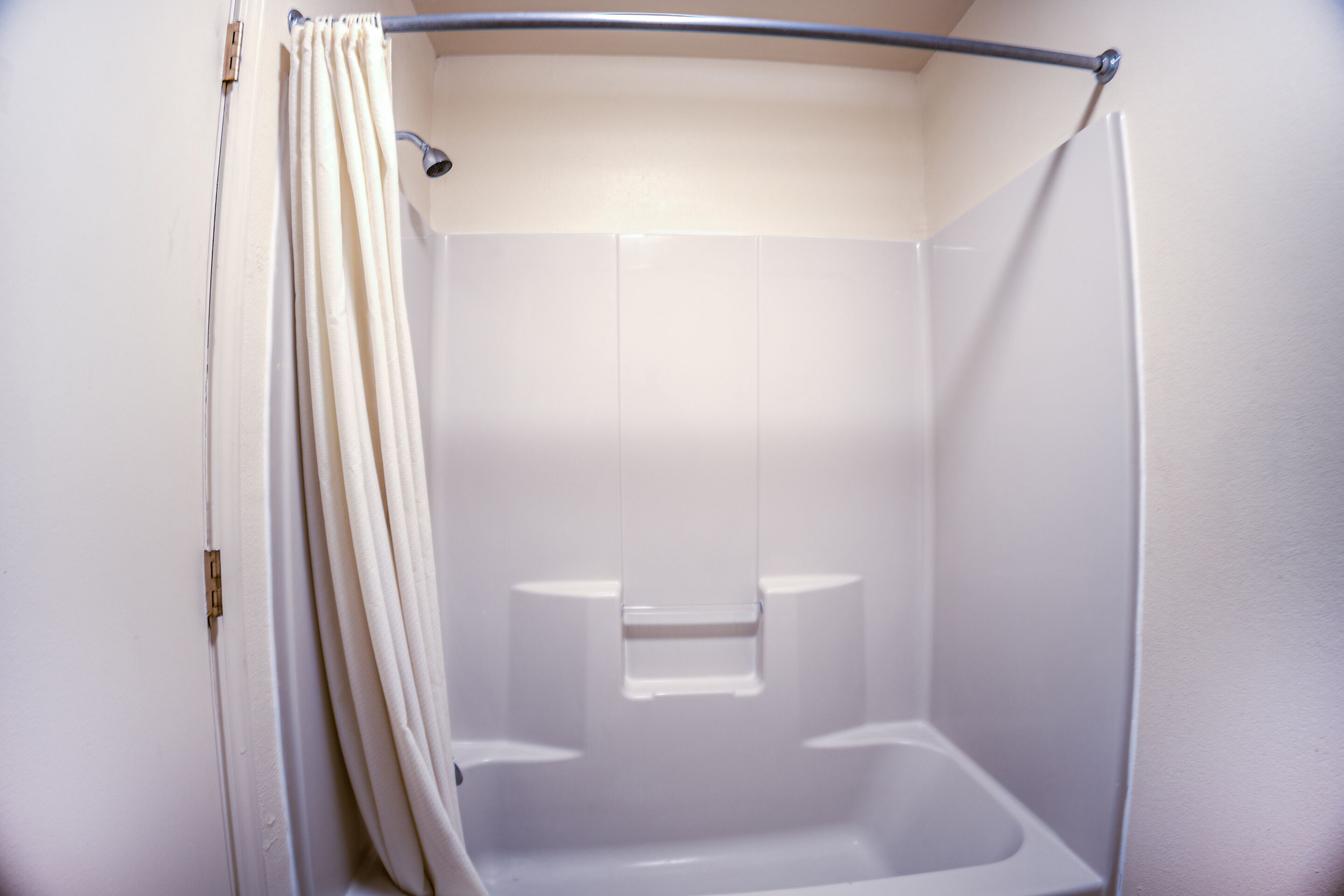 A shower with a curtain, a showerhead, and a tiled wall.