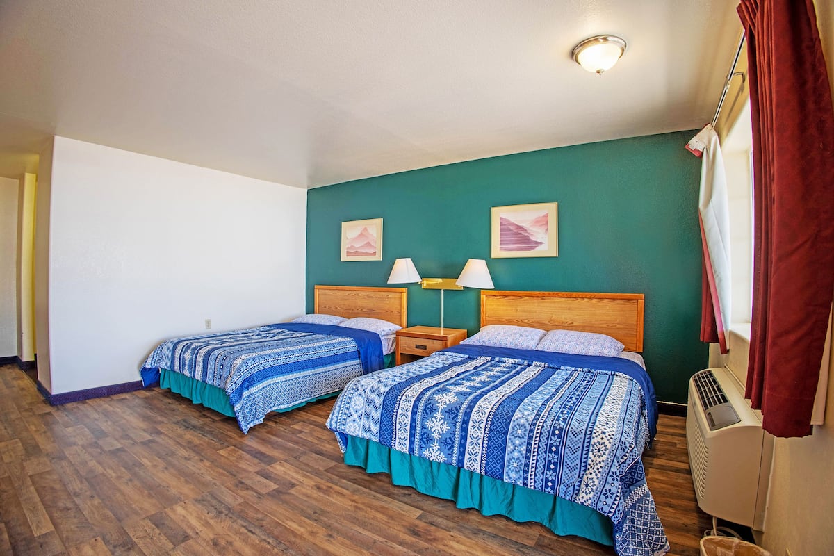 A room with two beds, wooden flooring, a green wall, and a ceiling light fixture.