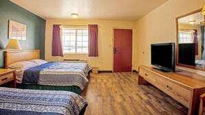 Une chambre d’hôtel avec deux lits, une télévision, une commode et une fenêtre avec des rideaux.