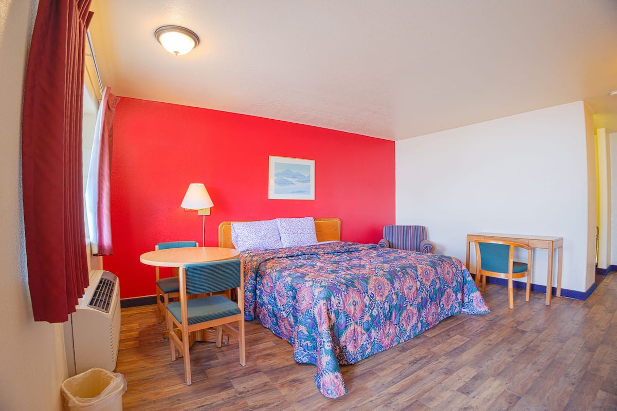 A room with a bed, a desk, a chair, a table, and a lamp.