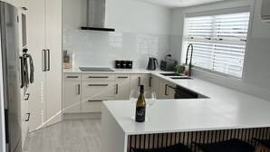 Een moderne keuken met witte kastjes, een centraal eiland met krukken, en een raam met zonwering.