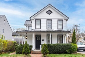 A two-story house with a black front door, a covered porch, and a small garden with trimmed bushes.