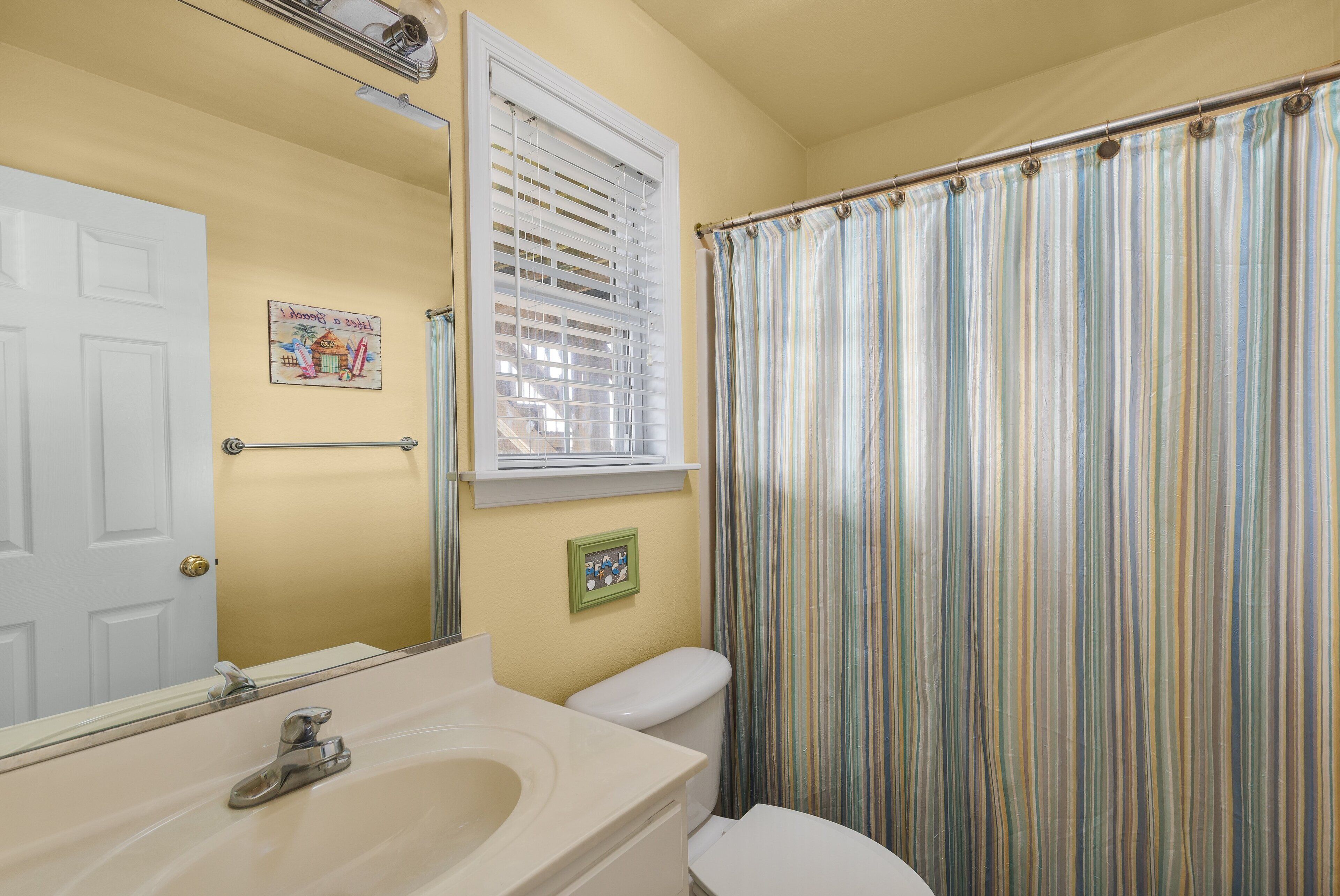 A bathroom with a toilet, sink, and a window with blinds.