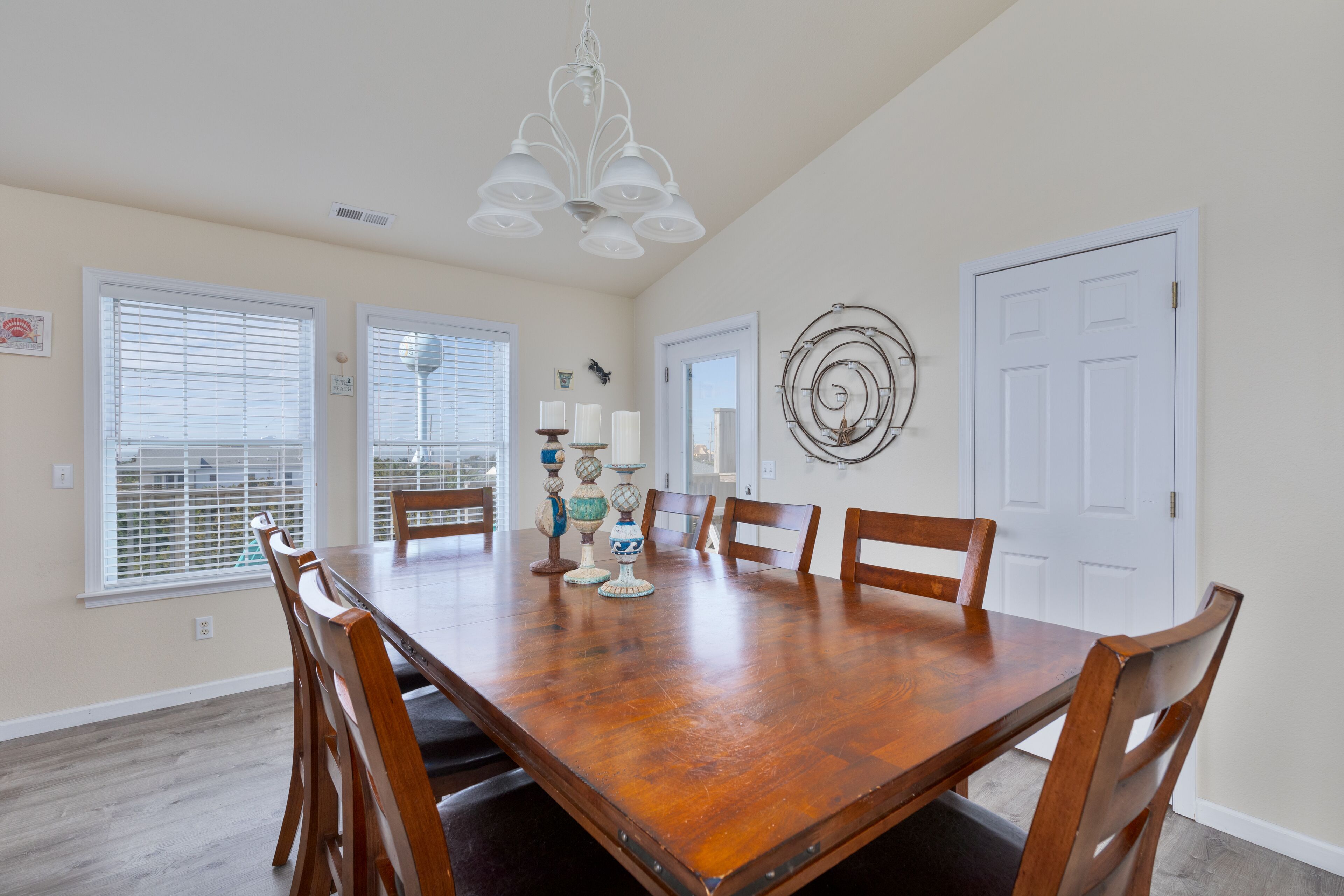 Un comedor con una mesa de madera, sillas, una lámpara de araña y objetos decorativos.