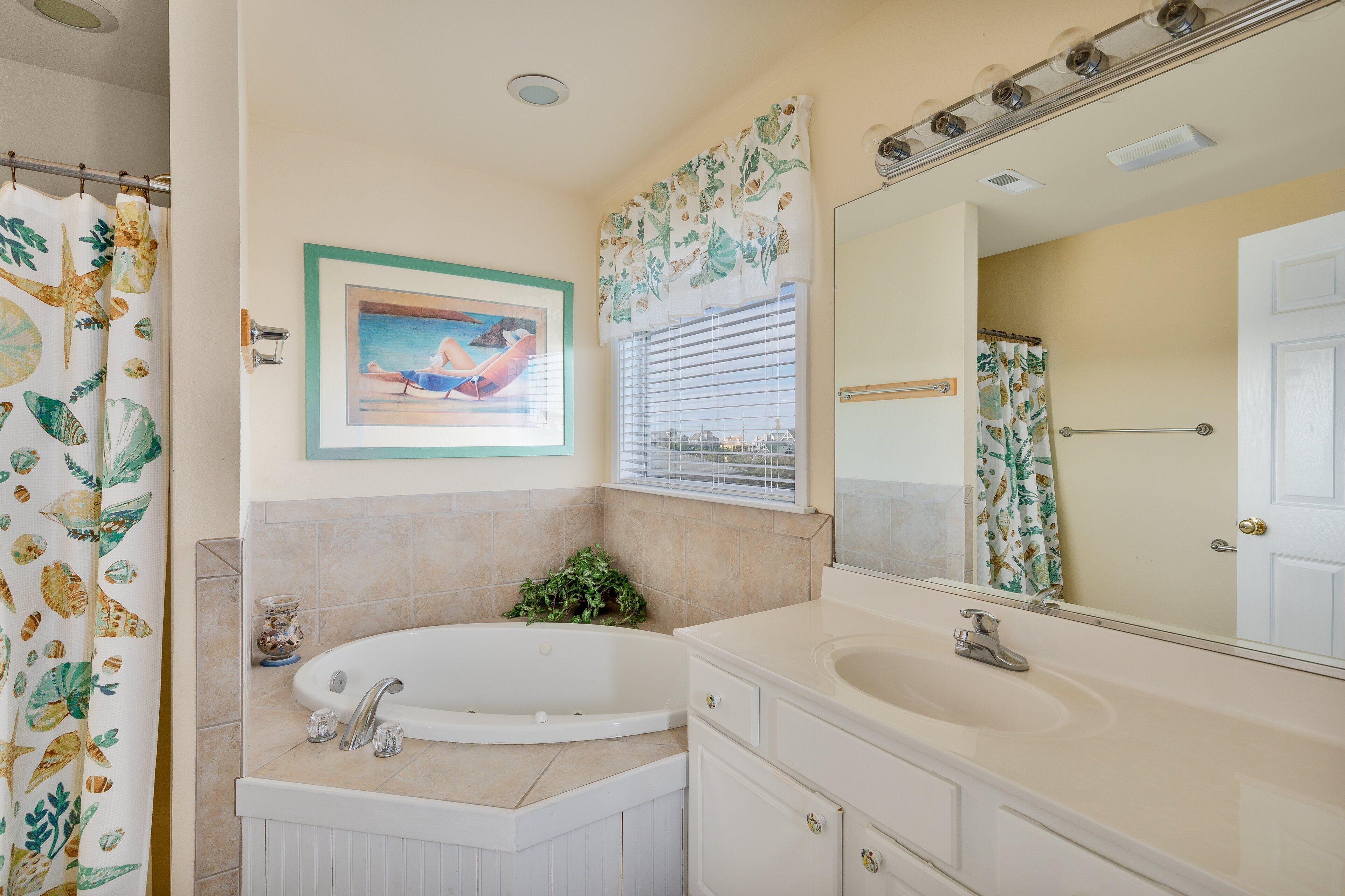 A bathroom with a bathtub, a sink, a mirror, and a shower curtain with a leaf pattern.