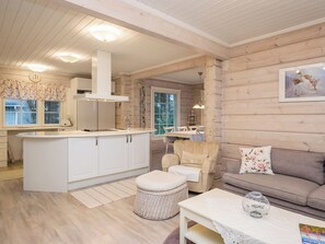 Eine moderne Küche mit weißen Schränken, einer zentralen Kochinsel und einem Essbereich inklusive Sofa und Sessel.