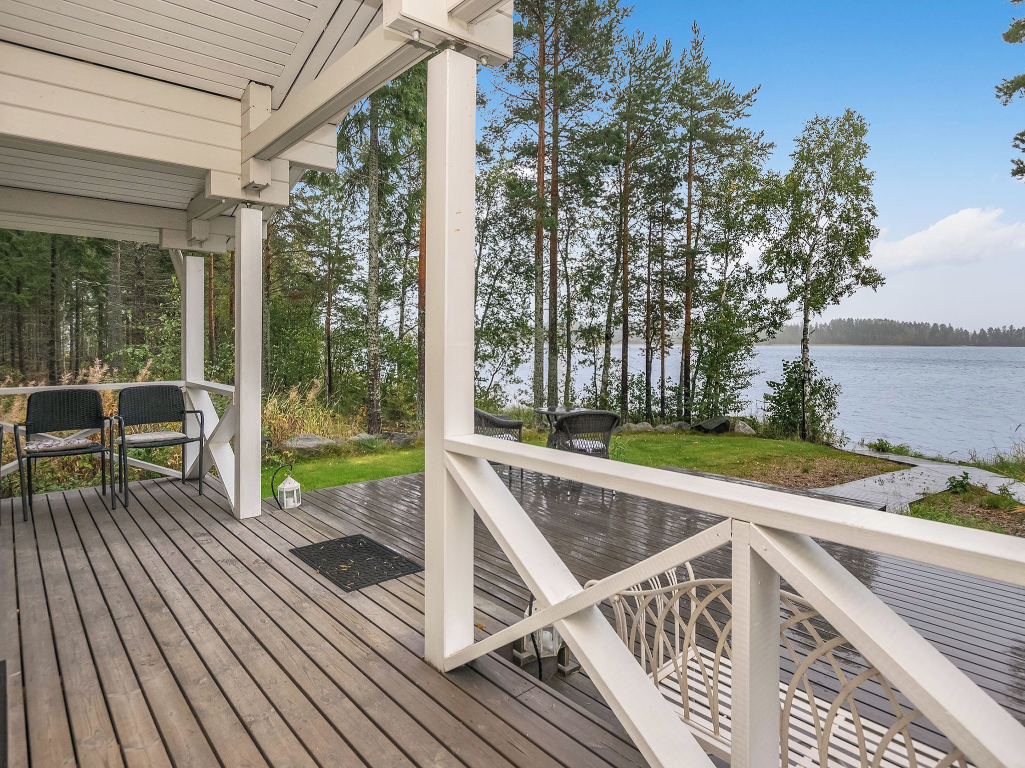 A wooden deck with outdoor furniture, overlooking a lake with trees and a distant shoreline.