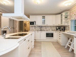 A modern kitchen with white cabinetry, a stainless steel sink, a built-in oven, and a microwave. - Tyssinniemi by Interhome (Punkaharju)