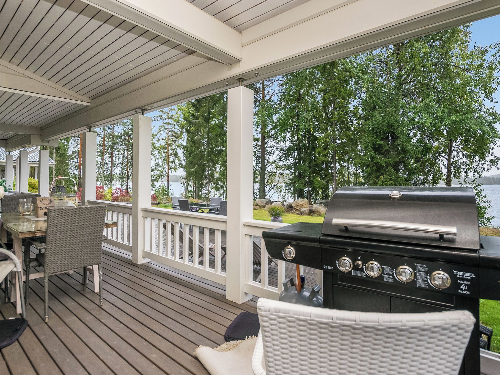 A covered deck with a grill, outdoor furniture, and a view of a lake.