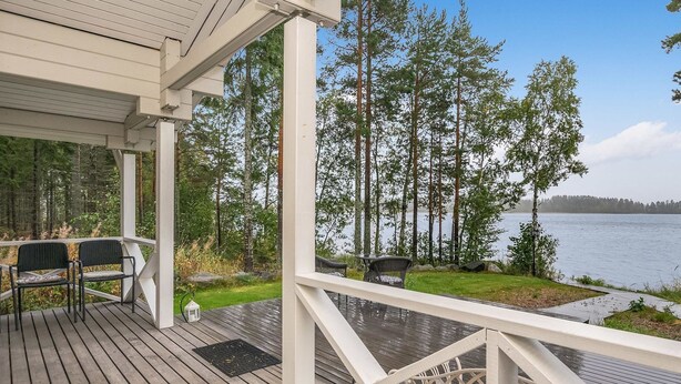 Eine Holzterrasse mit Gartenmöbeln und Blick auf einen von Bäumen umgebenen See.