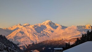 A mountain landscape with snow-covered peaks and a small building in the foreground.