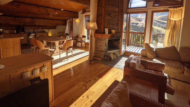 A spacious living area with a wooden ceiling, a stone fireplace, a dining table with chairs, and a sofa.
