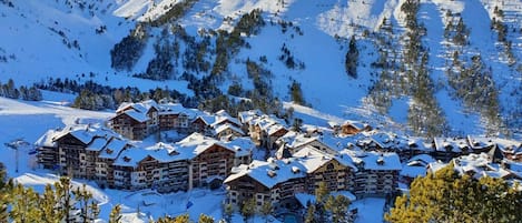 A snow-covered mountain resort with multiple chalet-style lodges, ski slopes, and a clear view of the surrounding peaks.