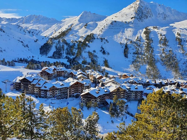 A snow-covered mountain resort with multiple chalet-style lodges, ski slopes, and a clear view of the surrounding peaks.