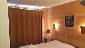 A room with a bed, a wooden wall, a painting, and a nightstand with a lamp.