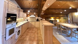 A kitchen with wooden cabinets, a built-in oven, a washing machine, and a dining area with a table and chairs.