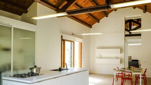 A modern kitchen with white cabinetry, a gas stove, and a dining area with red chairs. - Barbara by Interhome (Marsala)