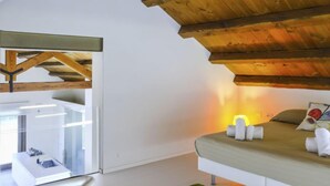 A modern bedroom with a sloped ceiling, a bed with pillows and towels, and a glass enclosure with a view. - Barbara by Interhome (Marsala)