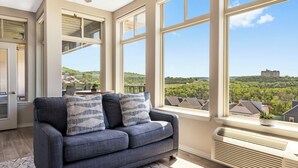A room with a large window, a ceiling fan, and a view of a distant building. - Lakeview Luxury • 3BR Majestic Condo • Sleeps 10 • Sunroom + Balcony (Branson)