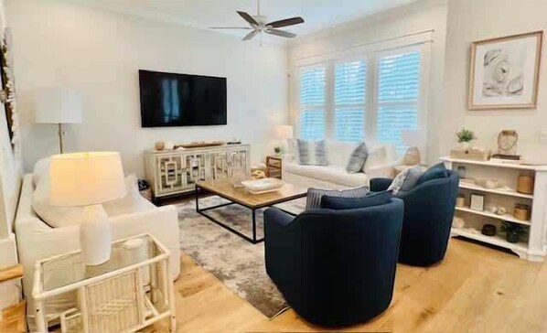 A modern living room with a white sofa, a dark armchair, a coffee table, and a TV mounted on the wall.