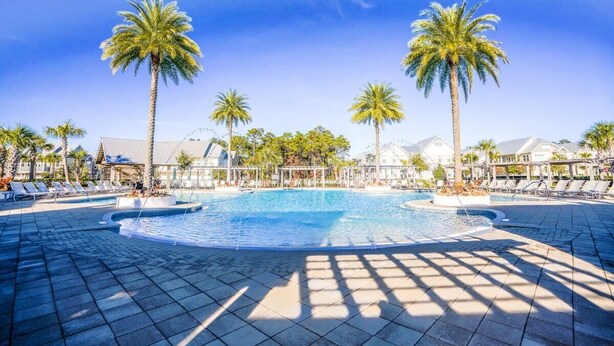 A resort pool area with palm trees, lounge chairs, and a clear blue sky.