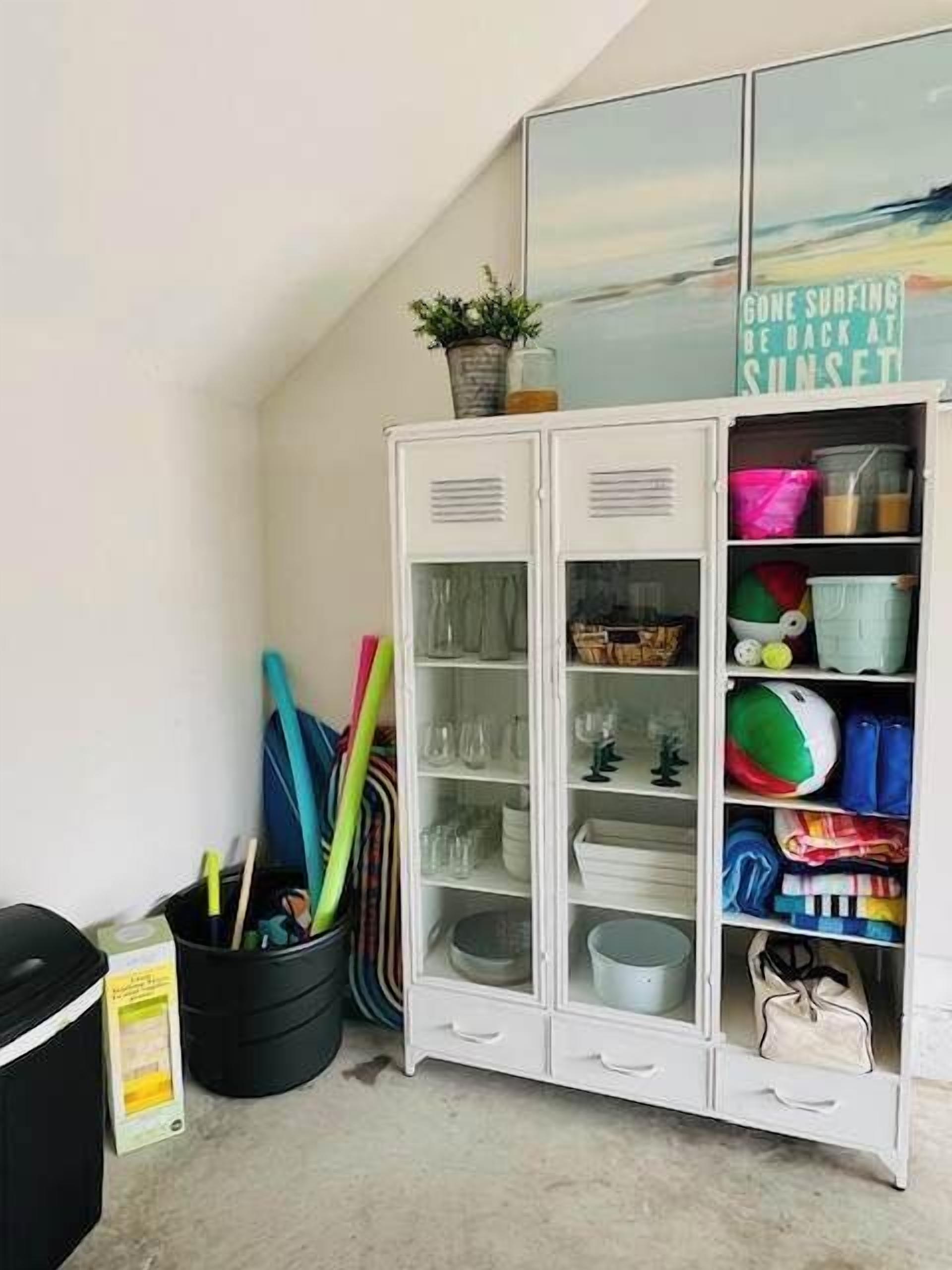 A white cabinet with glass doors containing various items, a black trash bin, and a sign on the wall.