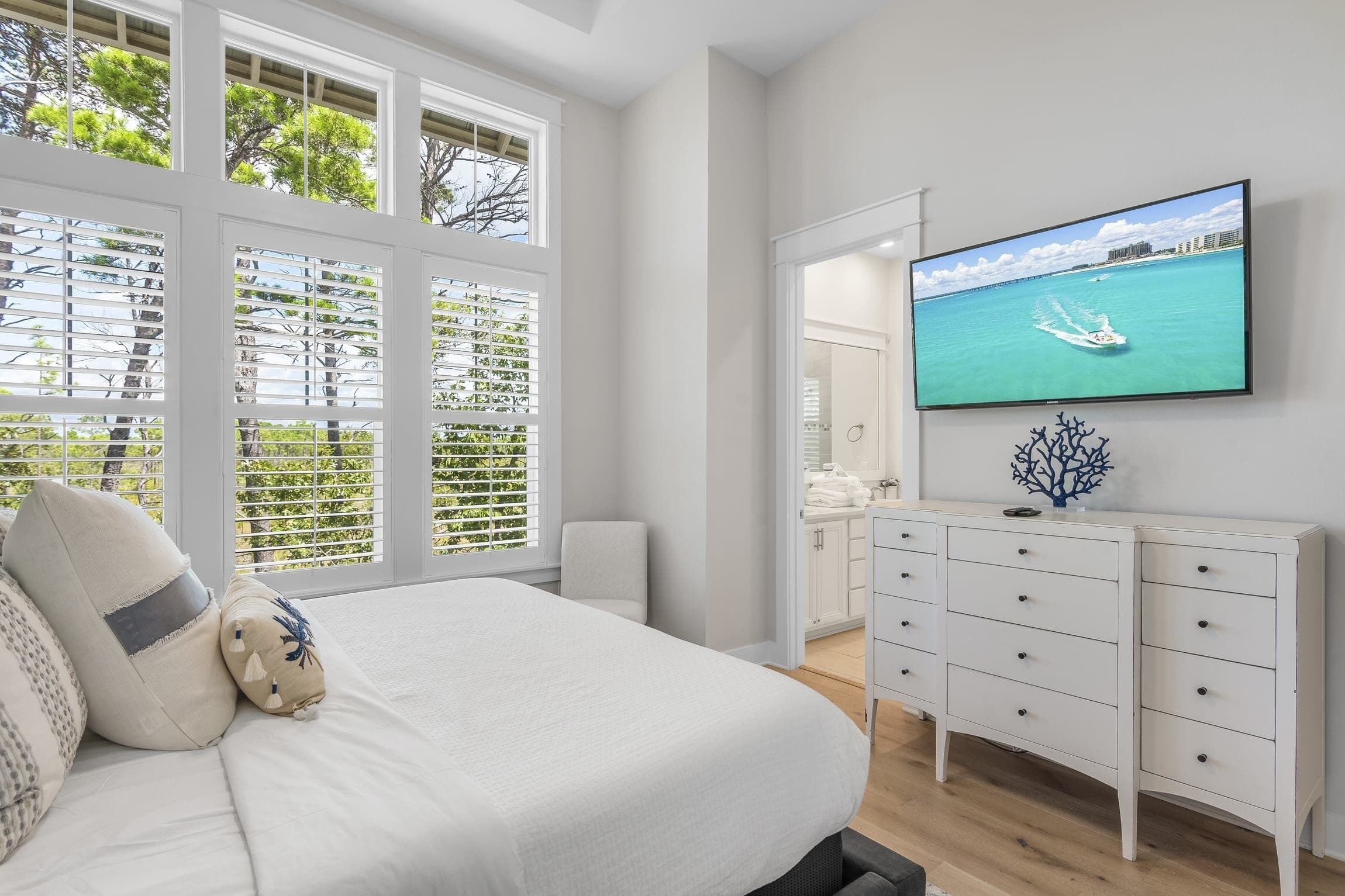 Une chambre avec un grand lit, un téléviseur fixé au mur et une vue sur la mer par la fenêtre.