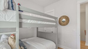 A bunk bed room with white bedding and a decorative mirror on the wall.