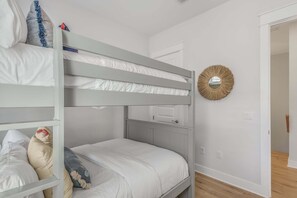 A bunk bed room with white bedding and a decorative mirror on the wall.