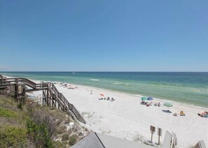 Ein Strand mit einer Holztreppe, die zum Sand führt, ein klarer blauer Himmel und das Meer im Hintergrund.