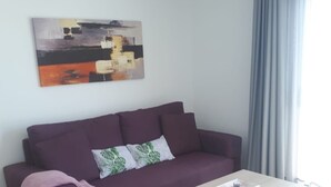 A modern living room with a purple sofa, a light-colored coffee table, and a matching ottoman. A painting is hung on the wall above the sofa. - FUERTEVENTURA PORT SEA (Morro Jable)