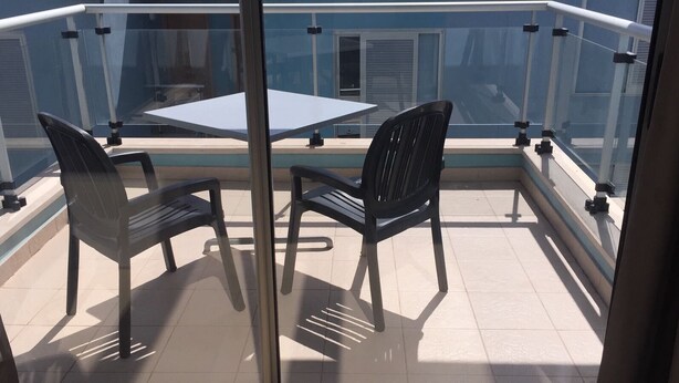 A balcony with two chairs and a table, a glass railing, and a view of a building. - FUERTEVENTURA PORT SEA (Morro Jable)