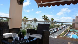 A balcony with wicker furniture, a pool, and a view of parked cars and palm trees. - ESQUINZO POOL AND BEACH (Esquinzo)