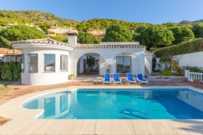 A poolside area with a pool, lounge chairs, and a building with a tiled roof.