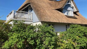 Een huis met rieten dak, een balkon en omringd door groen.