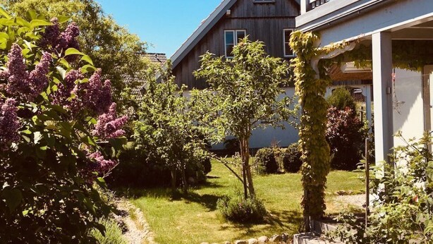 Een huis met schuin dak, een balkon en een tuin met diverse planten en een pad.
