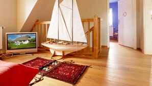 Een kamer met een houten vloer, een model zeilboot, een televisie en een kamerbreed tapijt met dessin.
