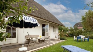 Een huis met rieten dak, een overdekt terras en een gazon.