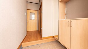Un couloir étroit au plancher en bois, une porte au fond et un meuble sur lequel est posé un vase.