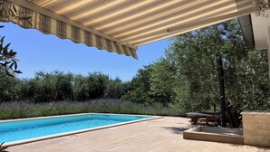 Une piscine dotée d’une terrasse en bois, entourée de verdure et agrémentée d’un patio couvert.