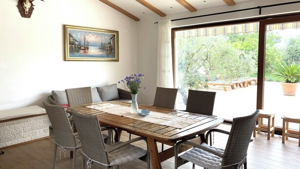 Un coin repas avec une table en bois et des chaises en osier, un tableau au mur et une vue sur la verdure à l’extérieur.