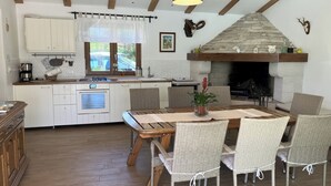Une cuisine avec des meubles blancs, une cheminée en pierre et un coin repas avec des chaises en osier.