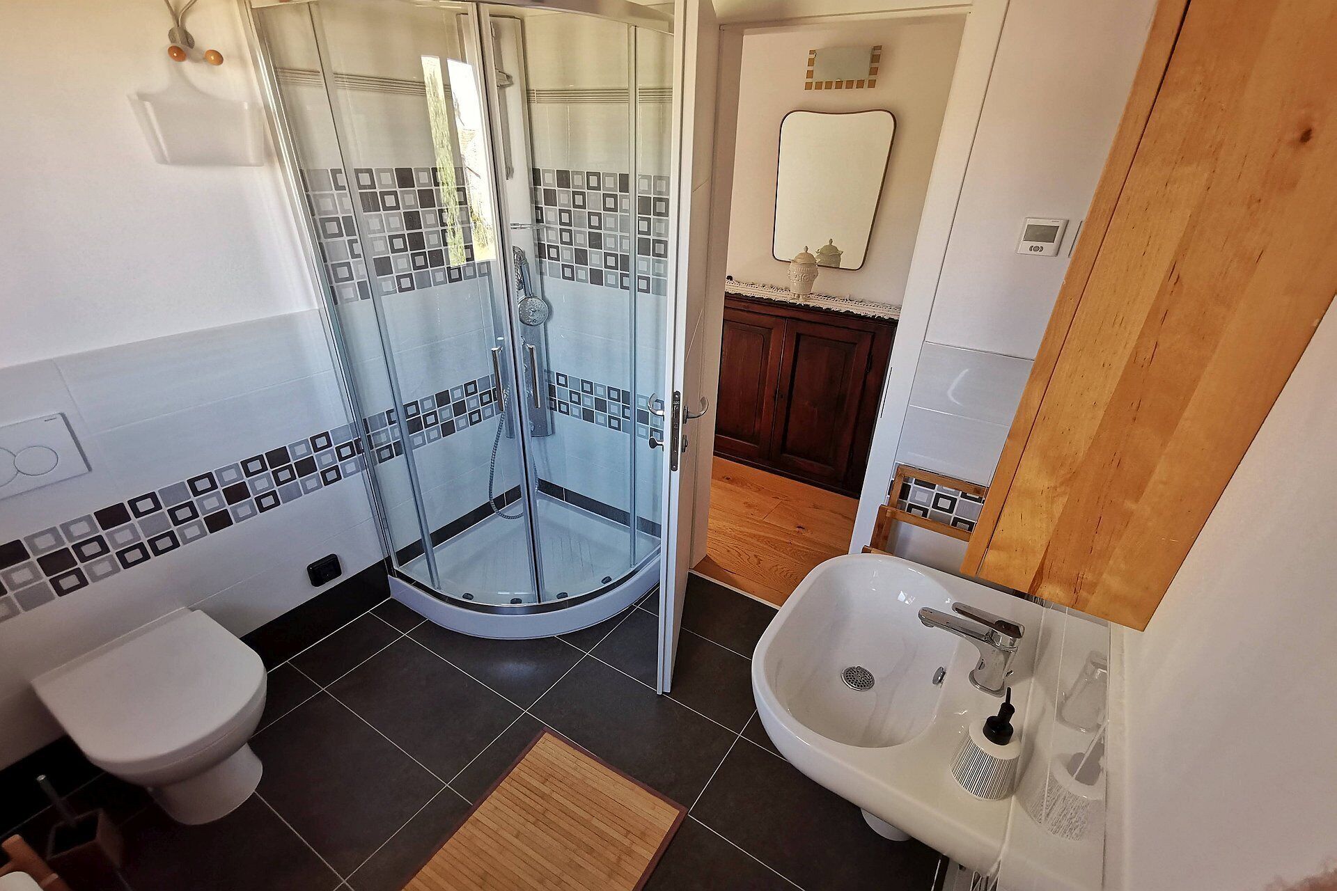 A bathroom with a glass-enclosed shower, a toilet, and a sink with a mirror above it.
