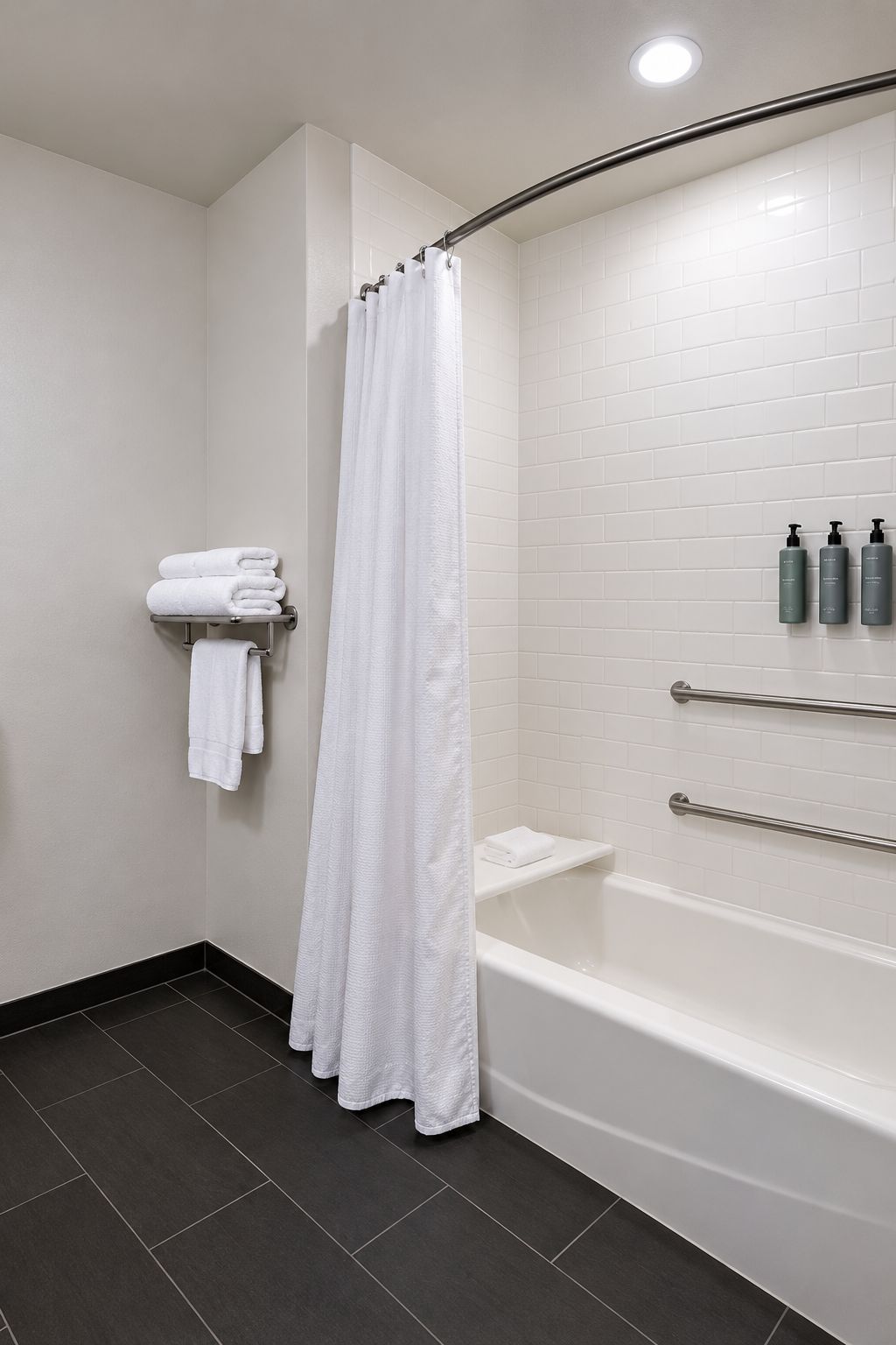 Un baño moderno con una bañera blanca, una cortina de ducha y un perchero con toallas dobladas.