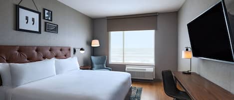 A hotel room with a large bed, a desk, a chair, a TV, and a window with a view.