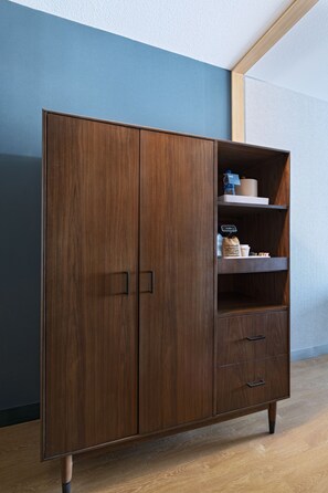 A wooden wardrobe with two doors and a shelf, placed against a blue wall. - Four Points by Sheraton Fort Worth North (Fort Worth)