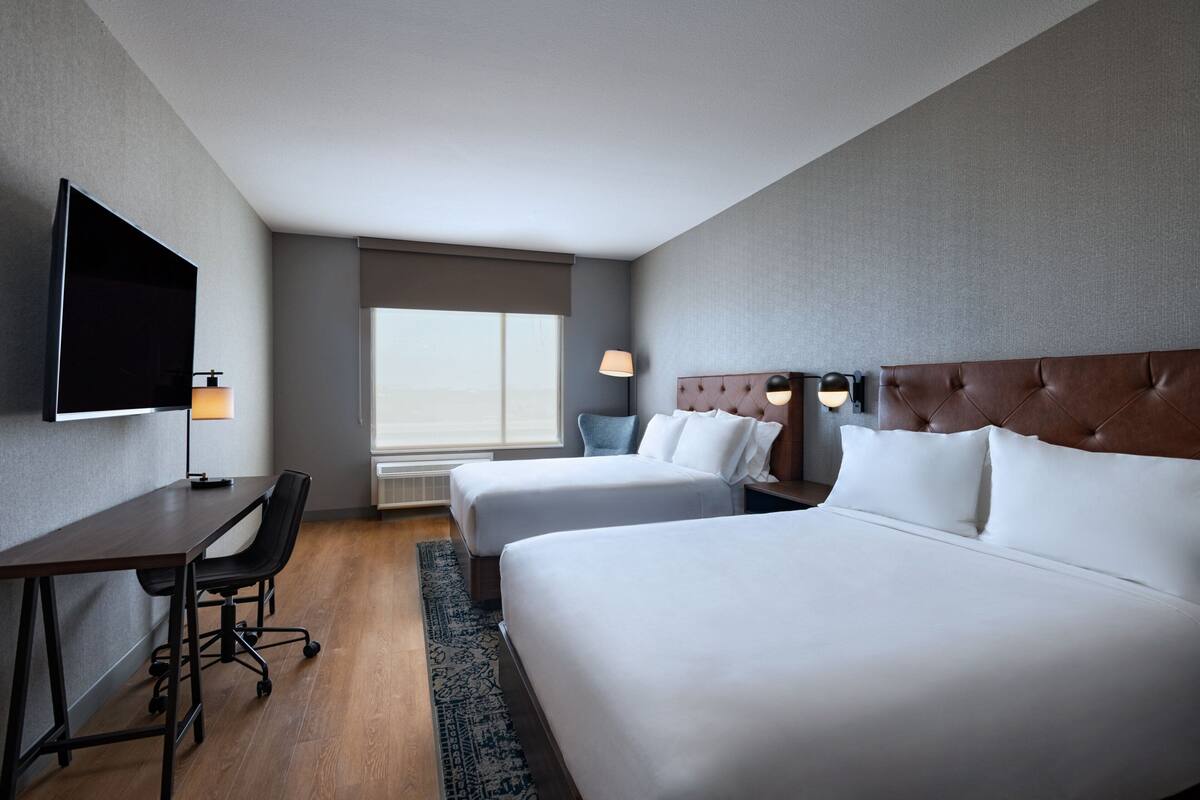 Habitació d'hotel amb dos llits, escriptori, cadira, televisió i finestra amb vistes.